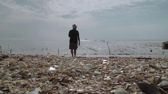 Low angle view a man walking over shells to the beach [4K]