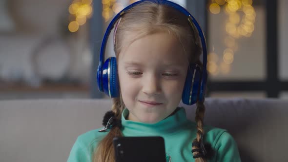 Little Girl in Headphones Enjoying Music on Phone