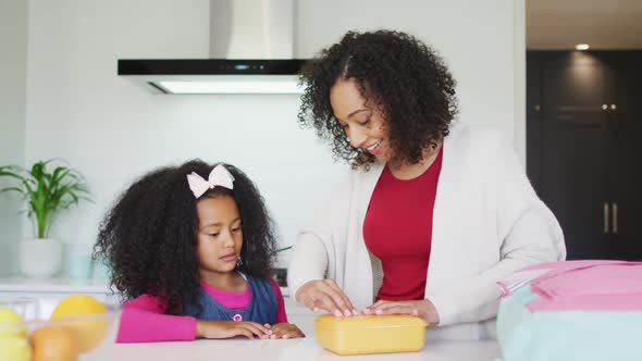 Happy african american mother packing lunch box for daughter to school