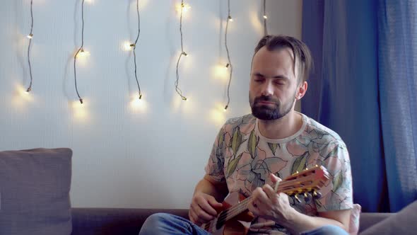 A bearded man  plays the ukulele