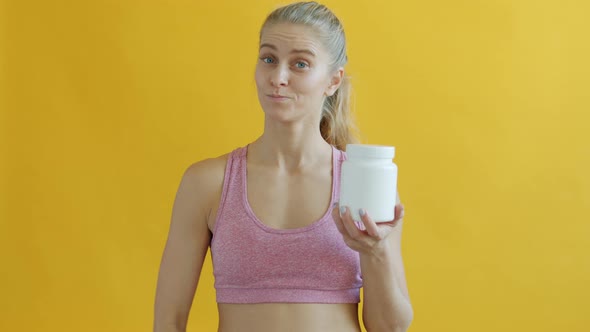 Portrait of Young Woman Holding White Jar of Sport Supplements and Showing Ok Hand Gesture