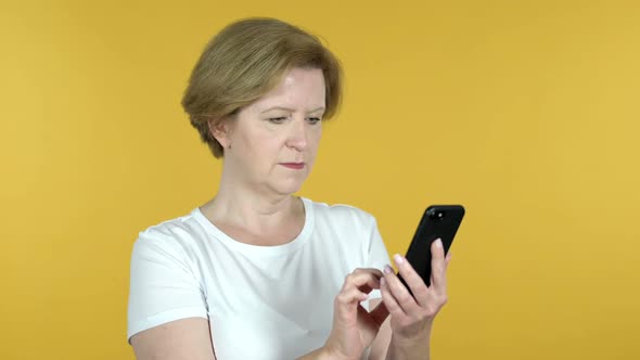 Old Woman Browsing Smartphone Isolated on Yellow Background
