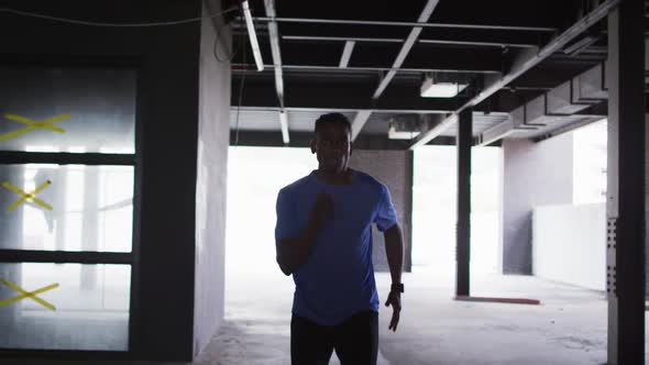 African american man wearing sports clothing jogging through an empty urban building