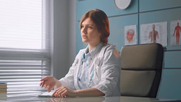 Young woman doctor in white medical coat talks to new patient and writes patient record