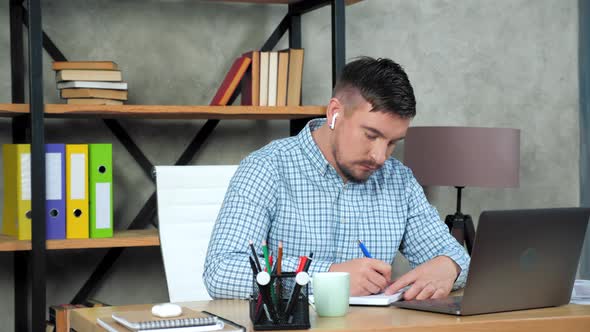 Businessman looks laptop writes information notebook, online video call meeting