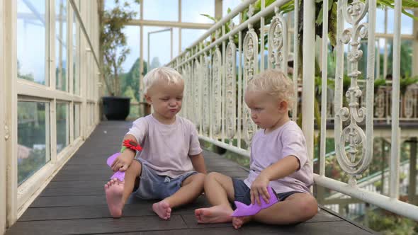 Two Adorable White Twin Toddlers Sitting and Playing Together Kiss Each Other