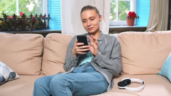 Young Woman Chatting on Smartphone on Sofa at Home