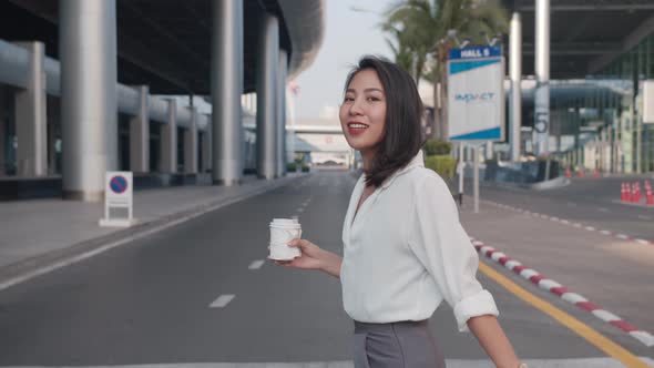 young Asia businesswoman holding disposable paper cup of hot drink and using smart phone while walk.