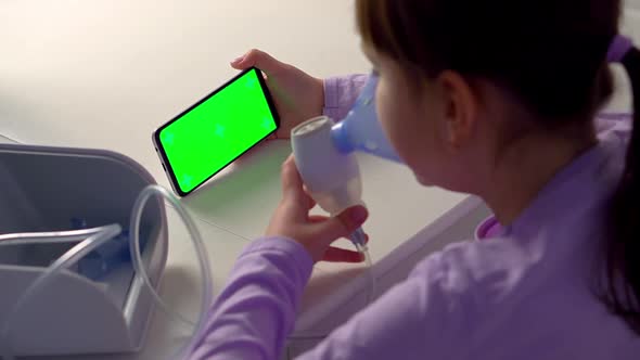 Little Girl is Sick Makes Inhalation with Nebulizer and Looks at Phone with Green Screen Mockup