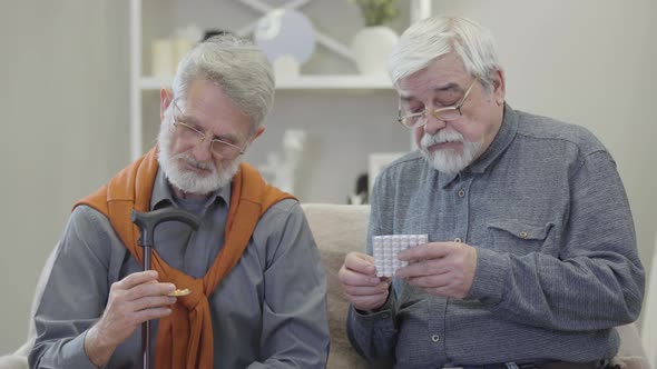 Portrait of Mature Caucasian Men Discussing Pills in Nursing Home. Two Serious Retirees in