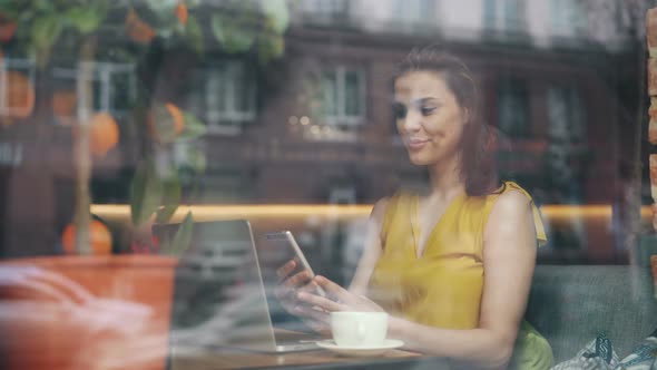 Pretty Young Woman Looking at Smartphone Screen Relaxing in Cafe Alone