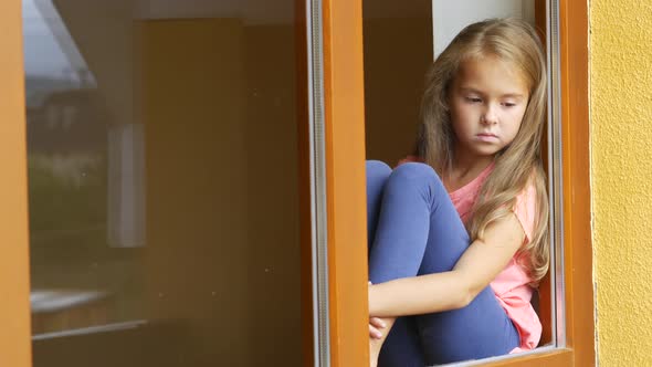 Sad Young Girl Looking Through a Window at Home