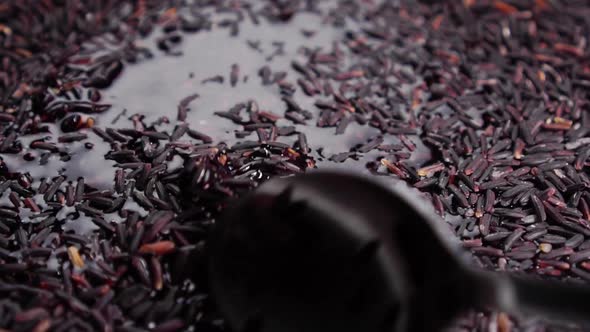 Cooking wild black rice. Stirring wet grains in water with a spoon in slow motion. Close-up