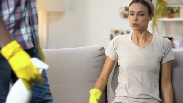 Tired Mixed-Race Couple in Gloves With Cleanser Spray Sitting on Sofa, Housework