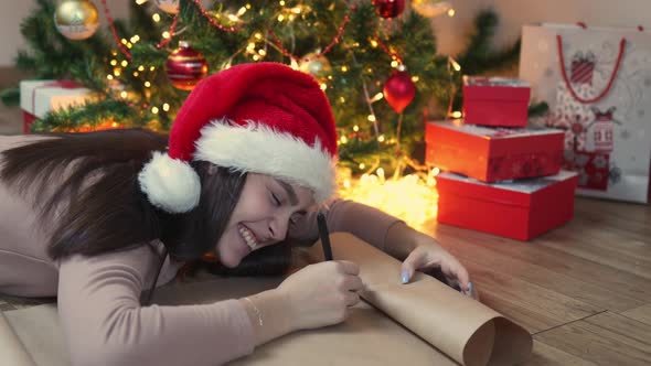 Brunette Woman in Red Santa Hat Writes Letter Christmas Tree Lights Gift Boxes