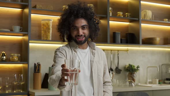 Muslim Man Stretches Hand Holding Glass of Water in Kitchen