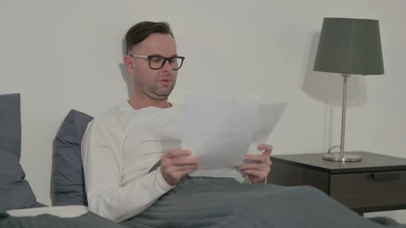 Casual Man Having Success on Documents While Sitting in Bed