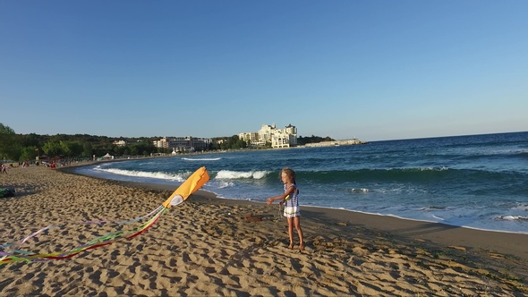 Little girl with flying kite on tropical beach at sunset. Kids play on ocean shore.