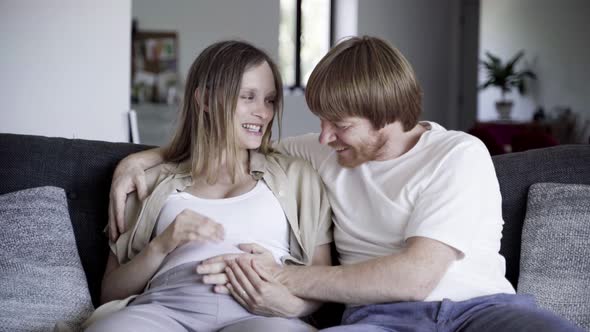 Happy Couple Sitting on Sofa and Touching Belly