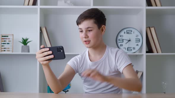 13 Years Old Boy Making Video Call Using Smartphone While Sitting at Table at Home