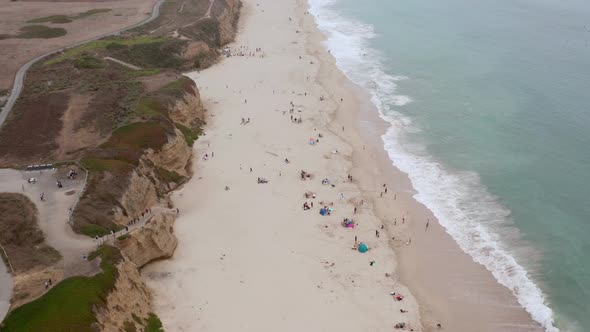 AERIAL: drone, half moon bay beach cliffs and people enjoying the beach, flying forward view