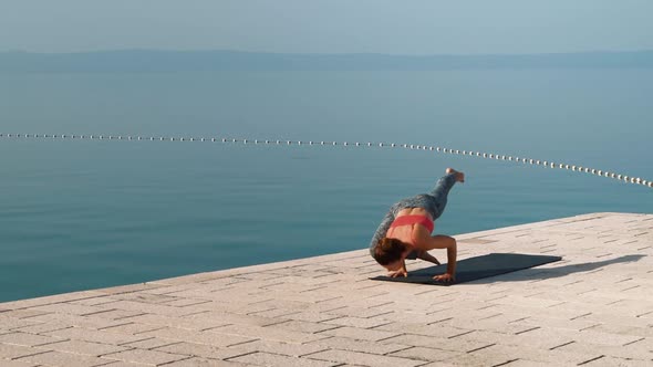 fit woman practices yoga on stone paving with sea and sky on background