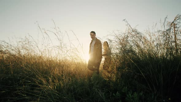 Couple Walks In A Field At Sunset