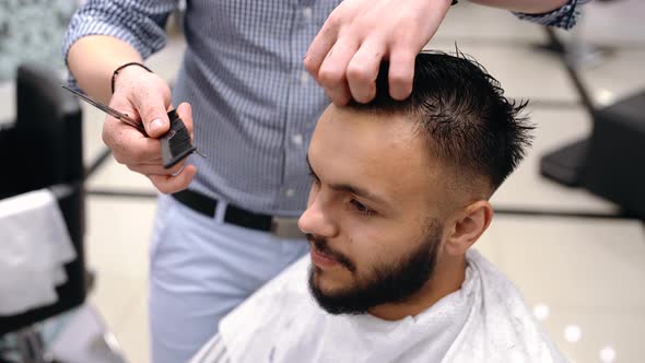 Unparalleled Barber with a Beard and a Tattoo Is Cutting the Hair of His Client in the Barbershop.