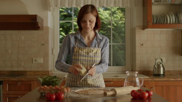 30s Woman Grating Cheese on Pizza Dough Standing in the Kitchen