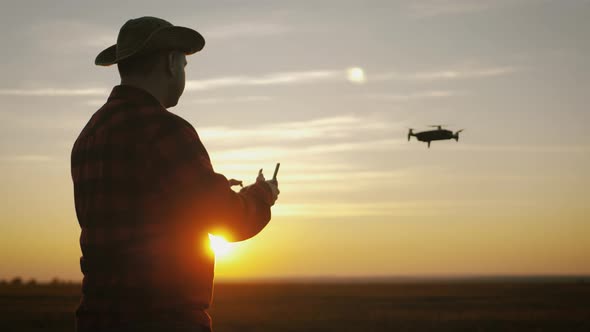 Silhouette of a Farmer Using a Drone in a Wheat Field at Sunset. Concept Technology Innovations for