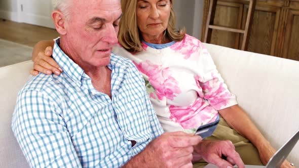 Smiling senior couple doing online shopping on laptop in living room