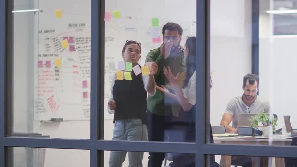 Diverse group of work colleagues brainstorming using glass wall in meeting room