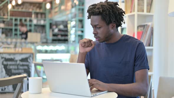 Coughing African Man Working on Laptop in Cafe