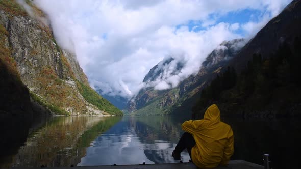 Male tourist wearing a yellow jacket sits down to enjoy the view on a quay. Impressive Landscape at