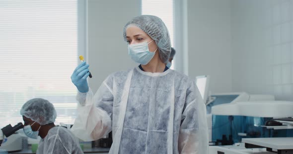 A Female Scientist Breaks Away From Examining a Test Tube and Looks Into Camera