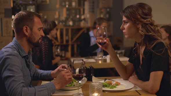 Caucasian Pair of Lovers Sitting at Restaurant Drinking Wine Eating Arguing While Group of People