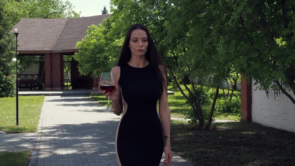 Elegant Woman with Glass of Wine Walking in Garden of Mansion