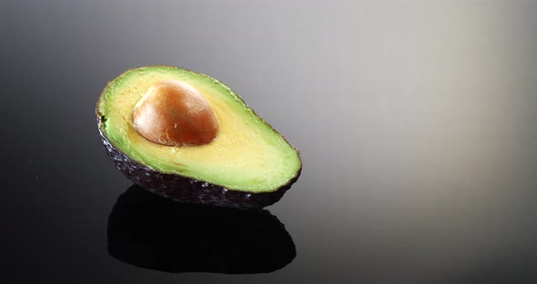 A ripe green avocado cut in half with the pit isolated on a black and white background.