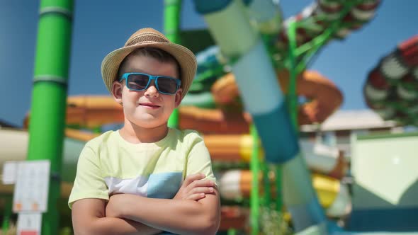 Smiling Trendy Cute Boy in Sunglasses and Hat Posing at Slide Open Air Aquapark Background