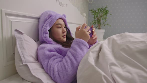 Young Adult Asian Woman Playing Video Games on Mobile Phone and Winning the Game Lying in Bed