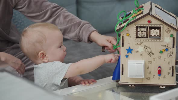 Mother and Her Baby Boy Playing with Wooden Busy House Montessori Educational Toy at Home