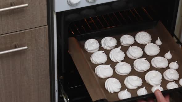 A Woman Puts A Baking Sheet With Meringue For A Cake In The Oven. Cake Count Ruins From Meringue