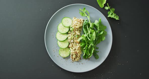 Video of fresh sliced cucumber, leaves and grains salad on grey plate over dark grey background