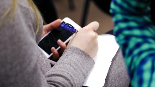 Woman is sitting and writing with a pen on a sheet of paper. Business woman holding phone