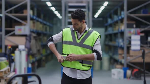 Handsome Bearded Middle Eastern Man Tying Velcro on Vest Standing in Industrial Warehouse and