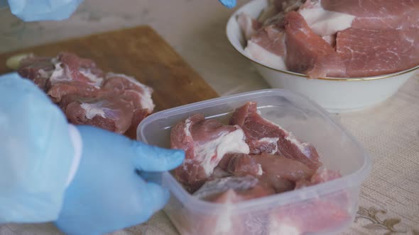 Cooking, Cutting Fresh Meat. Hands Dressed in Gloves and a Protective Disposable Blue Robe.