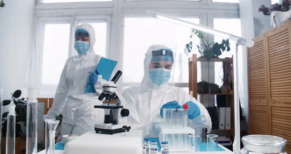 Focused Young Female Lab Scientist Doctor in Full Medical Protection Suit and Shield Works on New