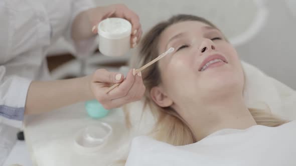 Close Up of Female Beautician Hands Holding Jar with Cream and Applying It Using Wooden Spatula to