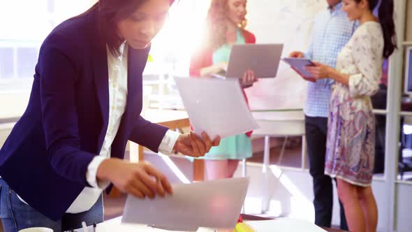 Businesswoman checking documents while coworker interacting in background