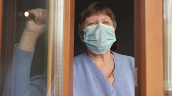 Woman on self-isolation at home by the window wearing a mask